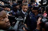 Police officers and members of the media surround Oscar Pistorius as he leaves court.