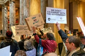 Protesters, some of whom are holding signs, gather outside the Senate chamber in the Minnesota State Capitol.