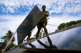 Employees install an array of solar panels on a roof.