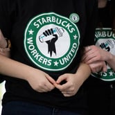 Three people wearing Starbucks Workers United shirts lock arms.