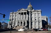 A cyclist passes by vehicles parked outside Colorado's Capitol building.