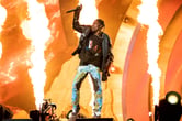 Travis Scott raises a microphone above his head while performing at the Astroworld Music Festival.