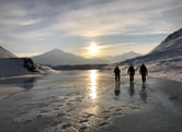 Three people walking on a glacial river in the Arctic.