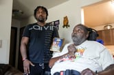 Myron Gates holds a photo of Travis King next to Carl Gates as the latter sits in a wheelchair in his living room.
