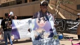 A man in a red, black, and white plaid shirt wearing a baseball cap and sunglasses stands with a poster of his daughter, Elisa Serna, who died in custody in a San Diego jail in 2019. Behind him are people with various other banners, including a larger Elisa Serna banner, in front of San Diego’s East County Superior Court in El Cajon.