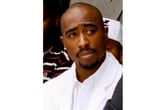 Tupac Shakur looks at something while wearing a white suit.