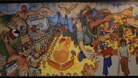 A large mural, depicting various scenes from a labor strike, including lines of picketing protesters and soldiers in gas masks.