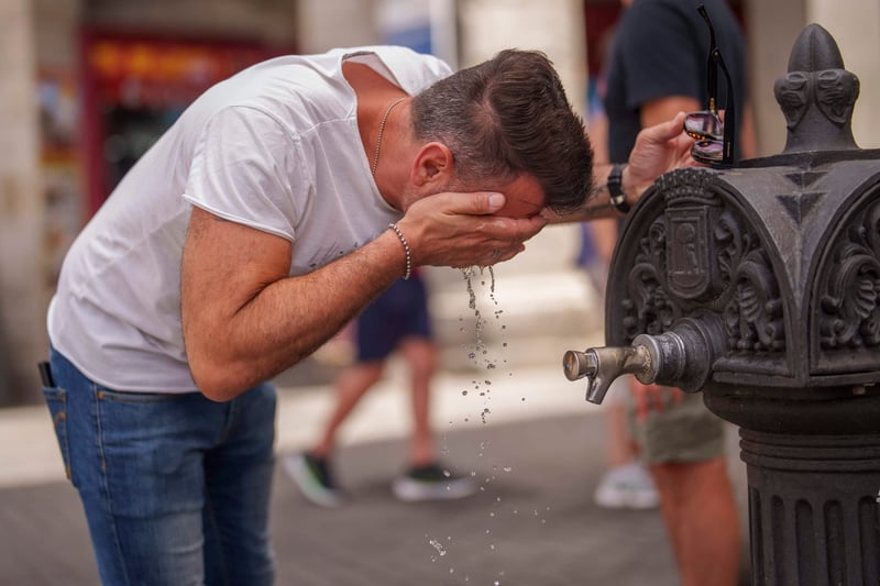A man splashes water from a fountain on his face.