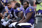 Michael Oher sits on a bench next to some of his Baltimore Ravens teammates during an NFL game.