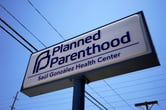 A Planned Parenthood sign below power lines on a sunny day.