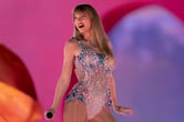 Taylor Swift holds a microphone in her right hand while performing on stage in a sparkly dress.