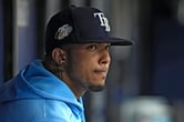Wander Franco wears a Tampa Bay Rays hat and sweatshirt while sitting on a bench in the team's dugout.