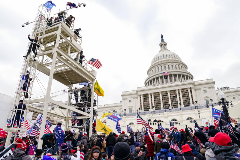 Insurrectionists holding American and Trump flags prepare to storm the U.S. Capitol.