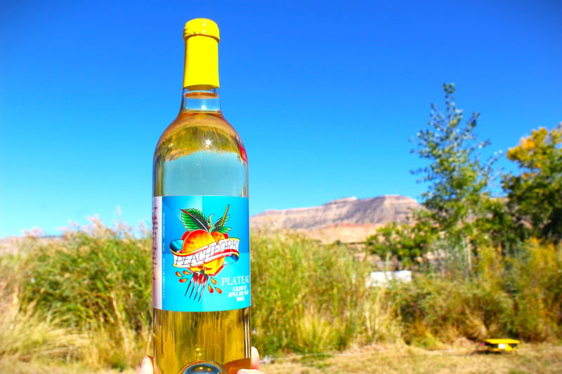 Yellow-topped bottle of Pear Apple Plateau wine with mesas and trees in the background