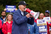 Joe Biden speaks into a megaphone in front of striking United Auto Workers holding signs.