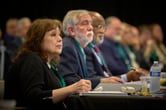 Minerva Carcaño writes in a notebook as she sits at a table next to several other people.
