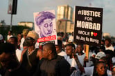 A group of people gather during a protest, with two of them holding signs referencing the mysterious death of Mohbad, in a street in Lagos, Nigeria.