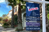A sold sticker on real estate-related signs outside a house with three palm trees in the front yard.