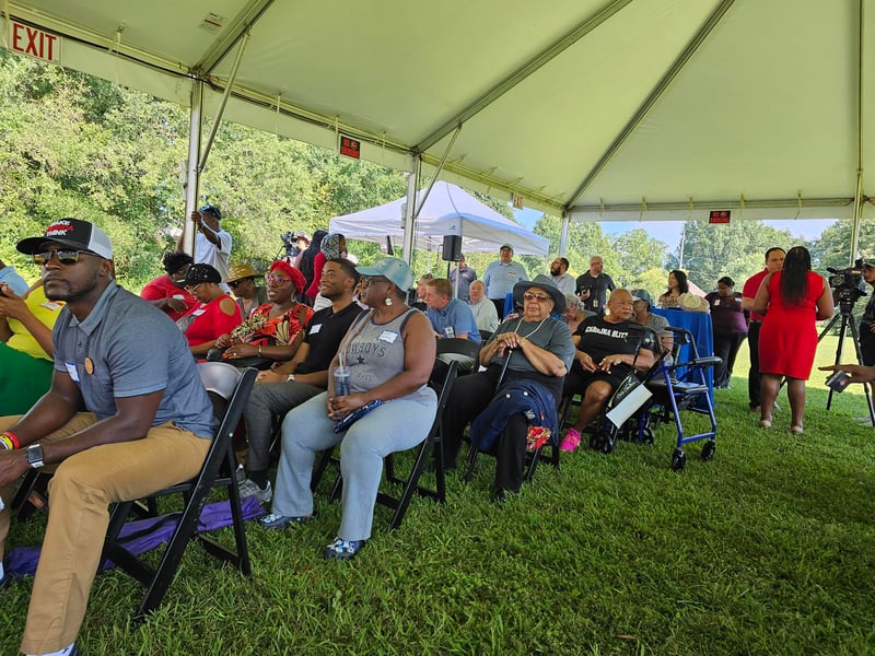 Residents of the Hoskins community of Charlotte gather beneath a tent to celebrate the sale of 32 homes that will be kept permanently affordable.