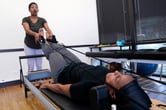 A health care worker helps a patient lying on a Pilates machine.