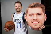 Luka Dončić poses for a photo while holding a basketball and a cardboard cut-out of his head.