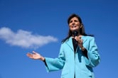 Nikki Haley holds a microphone in her left hand while speaking outdoors.