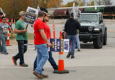 A Jeep SUV attempts to drive past strikers who are holding United Auto Workers-related signs while picketing.
