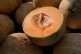 A pile of cantaloupes, with one of them cut in half.