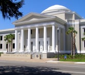 Tall palm trees flank either side of the beige and white Florida Supreme Court building in Tallahassee, Florida on a sunny day.