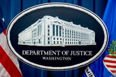 The Department of Justice seal in front of a blue curtain and two flags.