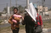 A woman holds up a stick with a white shirt on it as she walks with a man carrying a baby and another man as they flee Gaza City.