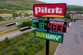 Several big rigs and a sedan drive along a freeway ner a a Pilot Travel Center sign.