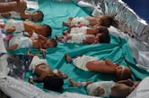A person cares for a premature baby on a table with eight other premature babies in a hospital.