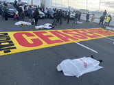 Protesters lie on a roadway covered in white sheets.