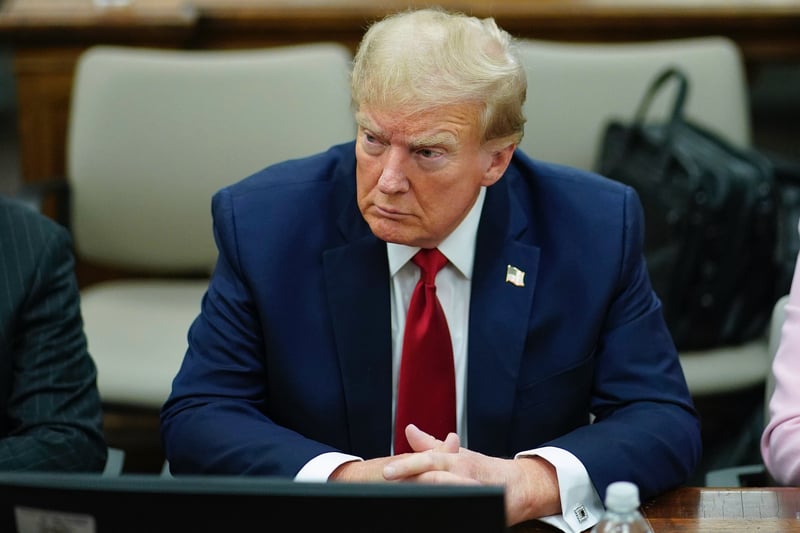 Donald Trump rests his hands on the defense table while sitting in a courtroom.