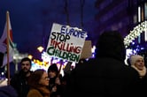 People holding a sign saying "Europe stop killing children" at night.