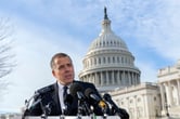 Hunter Biden speaks while standing behind a podium with seven microphones on it, with the U.S. Capitol in the background.