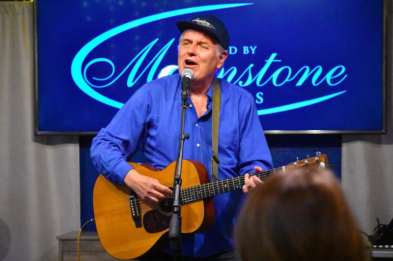 A man wearing a ball cap plays a guitar and sings.