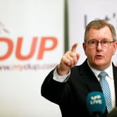 A man in glasses points at a news conference.