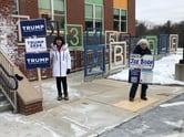 Two women hold signs outside an elementary school, one for Trump and the other for Biden.