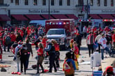 Dozens of Kansas City Chiefs fans stand around as emergency personnel respond to a shooting.