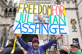 A man holds a banner reading "Freedom for Julian Assange."
