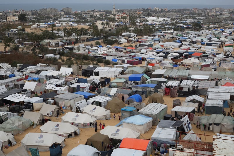 A large encampment of tents with people milling about, outside a city.