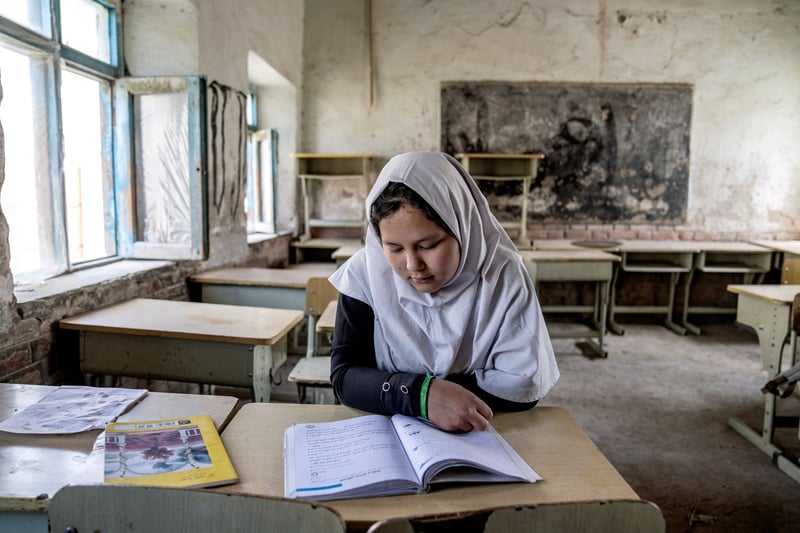 A girl in a headscarf at a desk in an empty classroom.