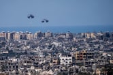 Parachutes drop over a city with bombed-out buildings near the sea.