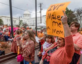 People protest at an IVF rally, including a mom with a sign holding her child.