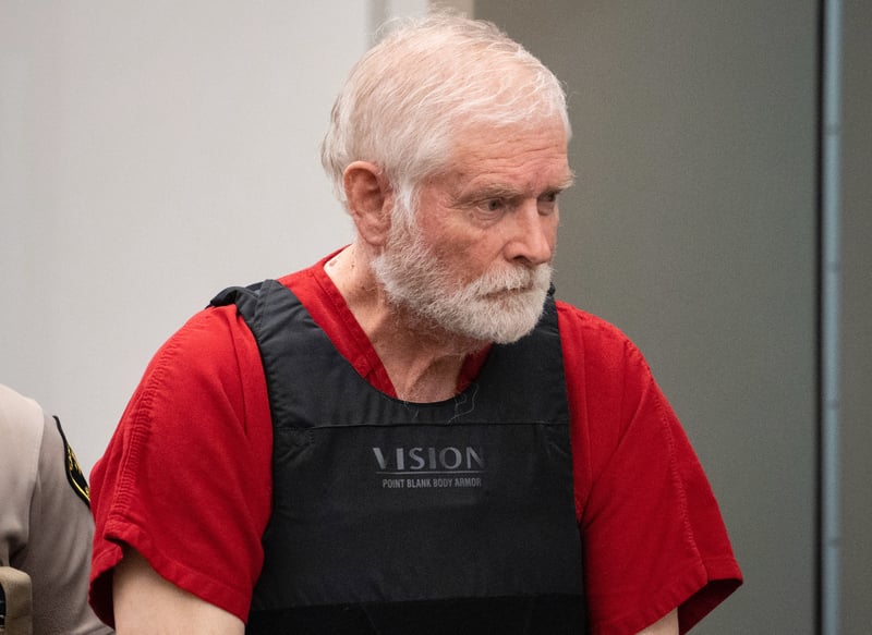 George Alan Kelly stands in court while wearing a black bulletproof vest over a red prison jumpsuit.