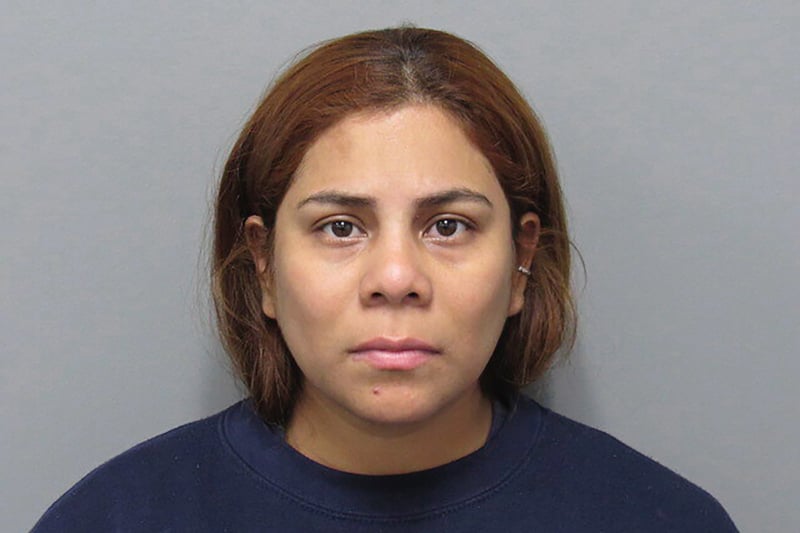 Kristel Candelario poses for a booking photo in front of a gray wall.