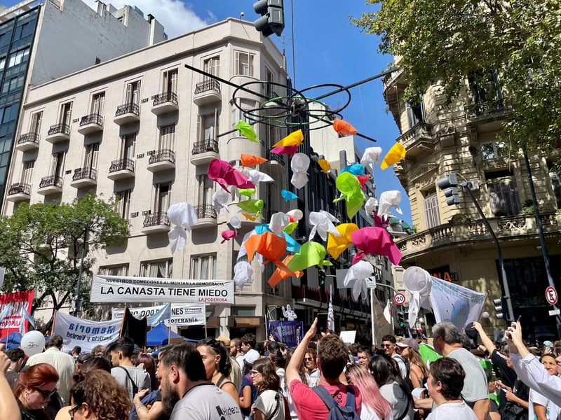 An instillation featuring handkerchiefs, a resistance symbol adopted by the Mothers and Grandmothers of the Plaza de Mayo during the dictatorship, hangs above a crowd.