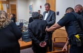 A bailiff escorts Muhammed Syed, who's handcuffed, inside a courtroom.